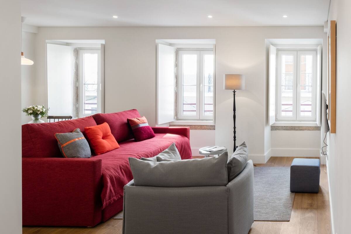 A modern living room with a red sofa, grey armchair, and a floor lamp.