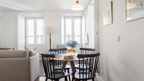 A modern, well-lit room with a dining area featuring a round table, four chairs, and a vase with flowers. - LSA Bairro Alto by Numa (Lisbon)