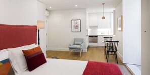 Un dormitorio con cama, una silla y una kitchenette al fondo.
