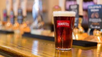 Una cerveza con etiqueta que dice "THWAITES" sobre la barra de un bar.
