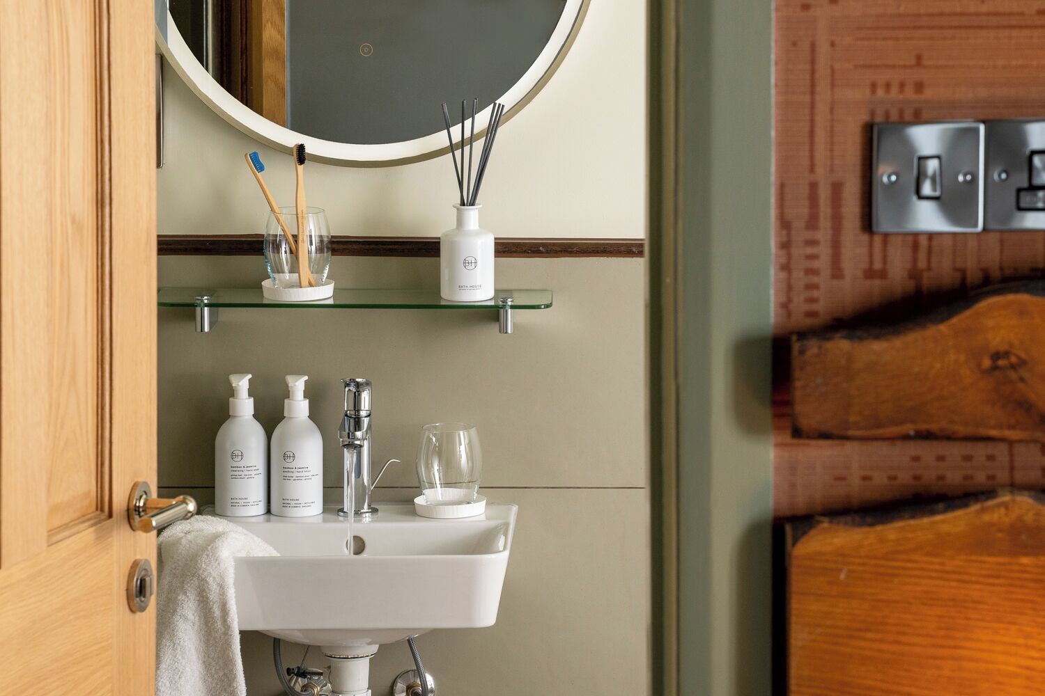 Une salle de bain avec un lavabo blanc, un miroir et des étagères contenant des articles de toilette.