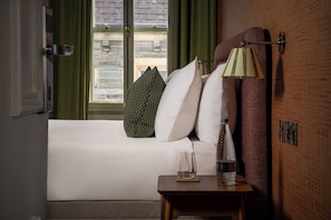 Ein Hotelzimmer mit Bett, Kissen, Nachttisch mit Glas, Flasche und Lampe.