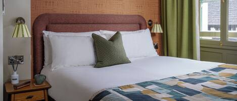 A neatly made bed with a patterned quilt, a wooden nightstand with a lamp, and a patterned wall.
