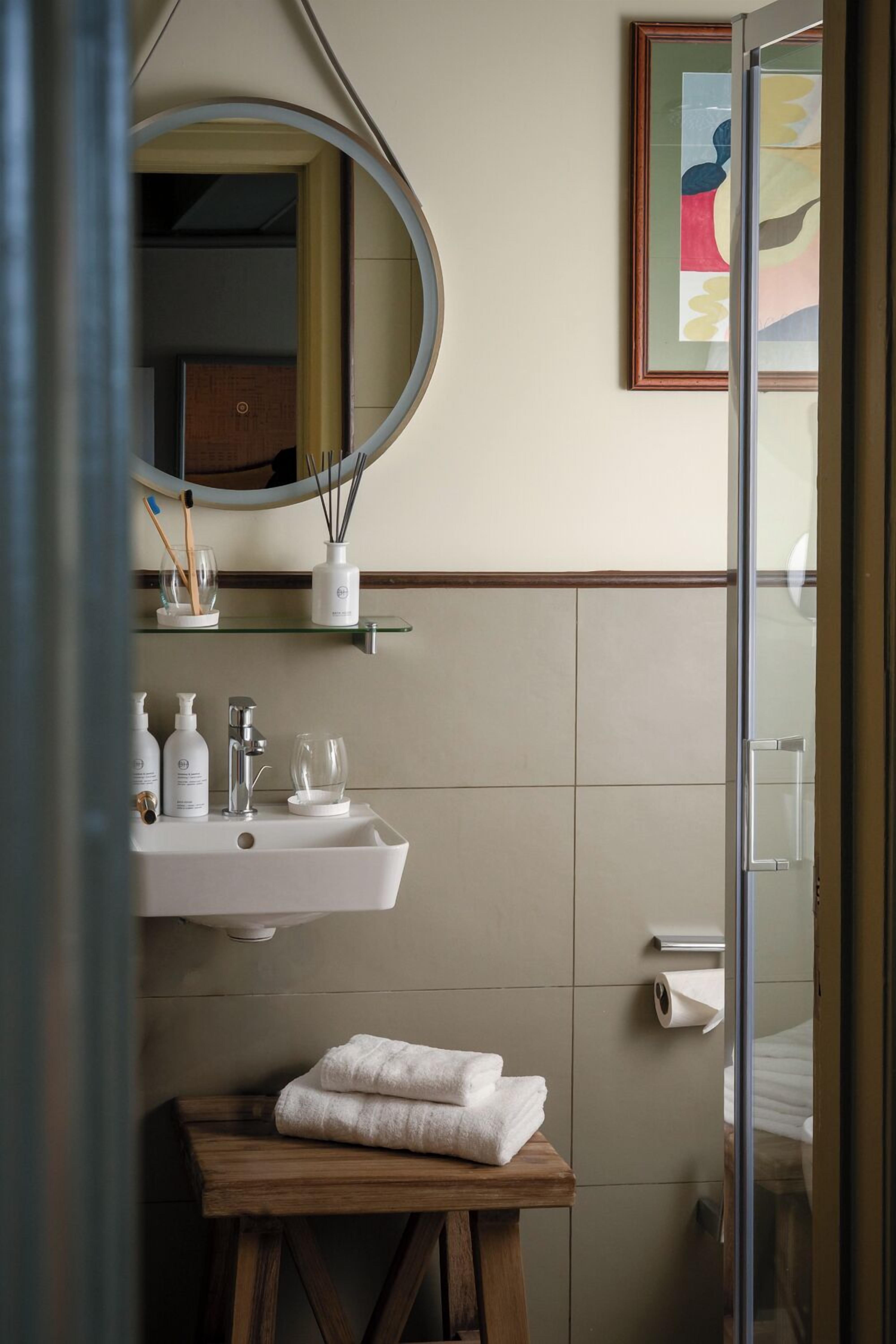 Un baño con lavamanos blanco, espejo y toallero.