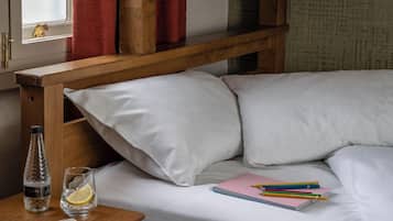 Ein Etagenbett mit weißer Bettwäsche, ein Nachttisch aus Holz mit einer Flasche und Gläsern sowie ein rosa Notizbuch.