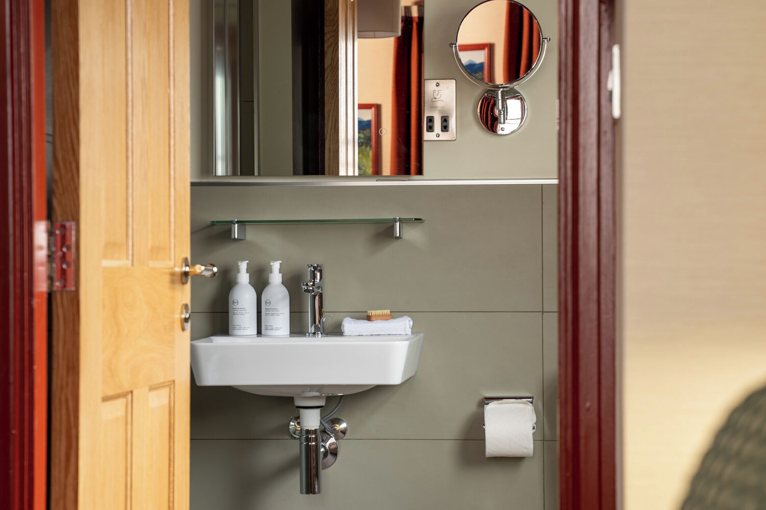 A bathroom with a white sink, two bottles of shampoo, a mirror, and a towel.