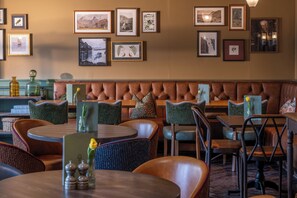 A restaurant with a leather booth seating area, round tables, and various framed pictures on the walls. - Royal Oak at Keswick (Keswick)