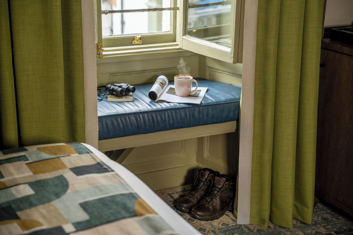 A bunk bed with a window, a book, a mug, and a pair of boots.