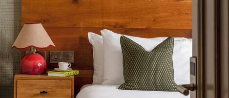 A hotel room with a wooden headboard, a bedside table with a lamp, a quilted pillow, and a book.
