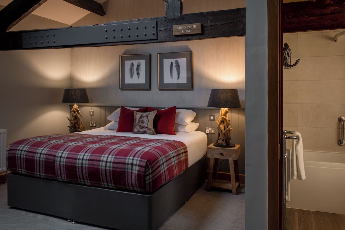 A bedroom with a large bed, two framed pictures on the wall, a wooden headboard, and a nightstand with a lamp.