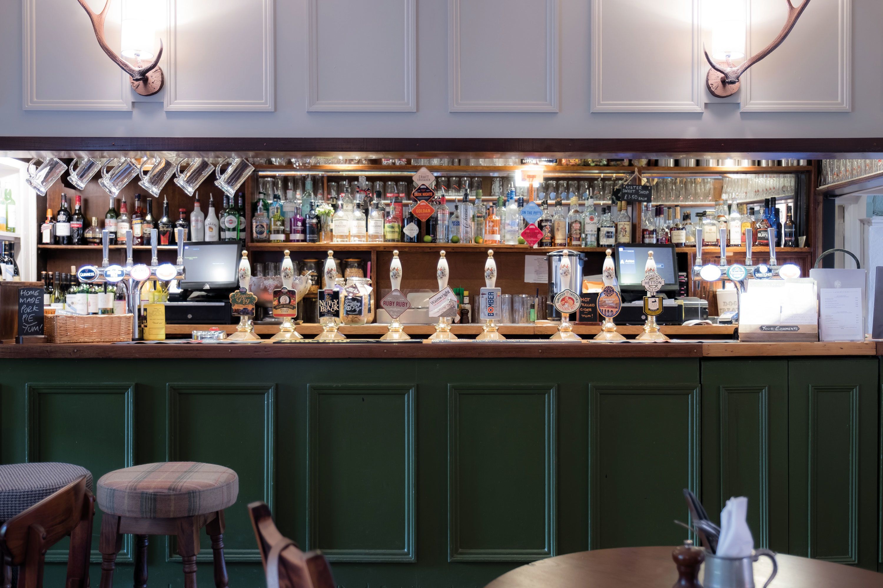 Eine Bar mit einer Holztresen, zahlreichen Flaschen und einem Computermonitor.