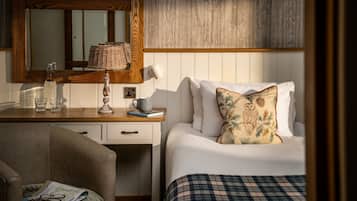 Un dormitorio ordenado con cabecera de madera, mesita de noche con lámpara, espejo y cama con manta escocesa y cojín decorativo.