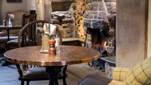 A round table with a copper finish, a glass vase with utensils, and a candle holder. - Lister Arms (Skipton)