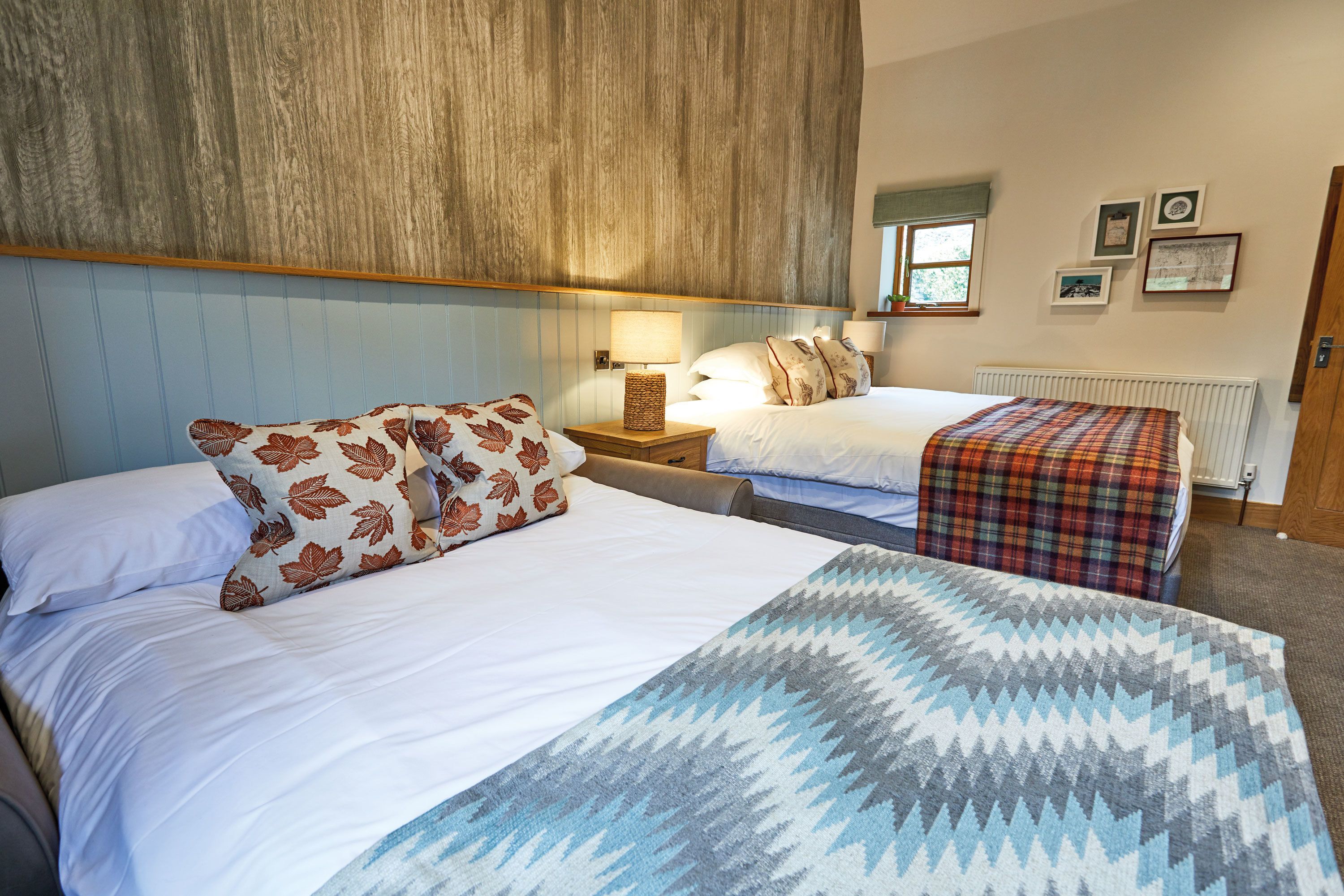 A hotel room with two beds, a wooden headboard, a window with a view, and a wall with framed pictures.