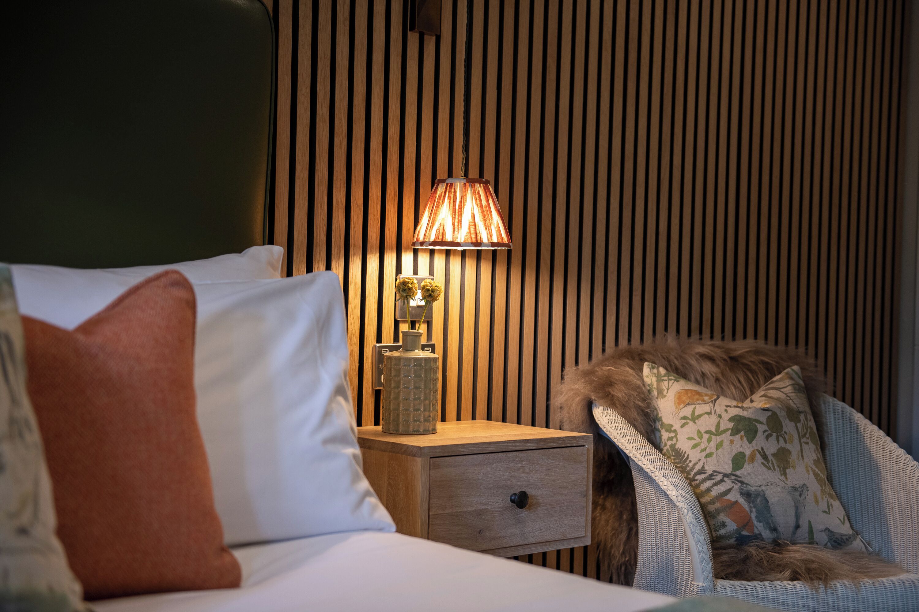 A neatly made bed with a pillow, a bedside lamp, and a small wooden nightstand with a decorative vase.