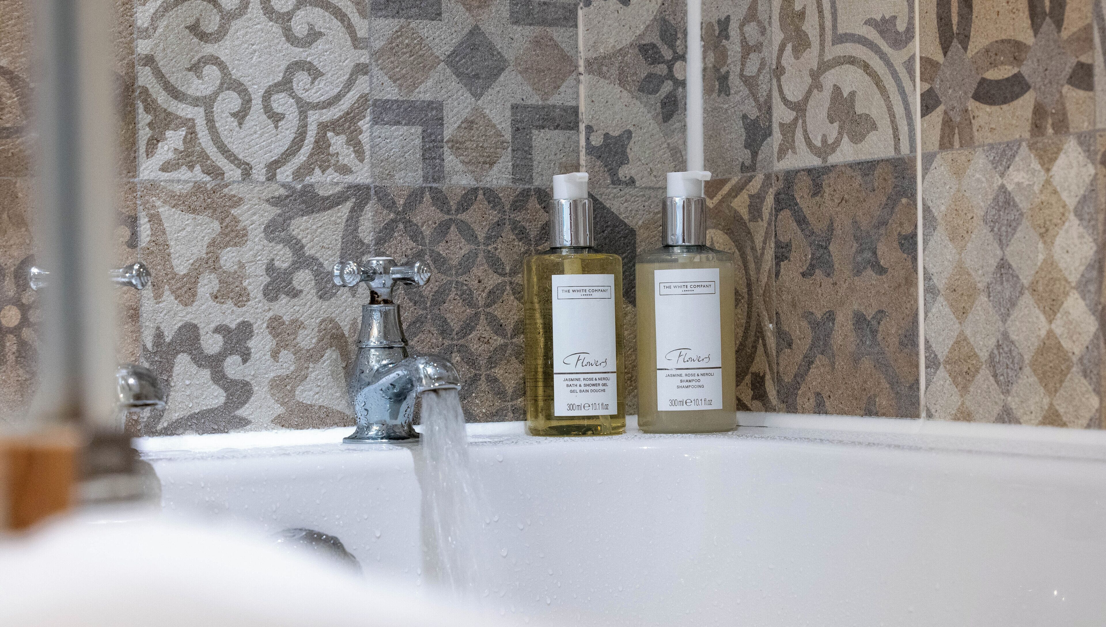 Un baño con bañera, grifo y dos productos de baño de The White Company.