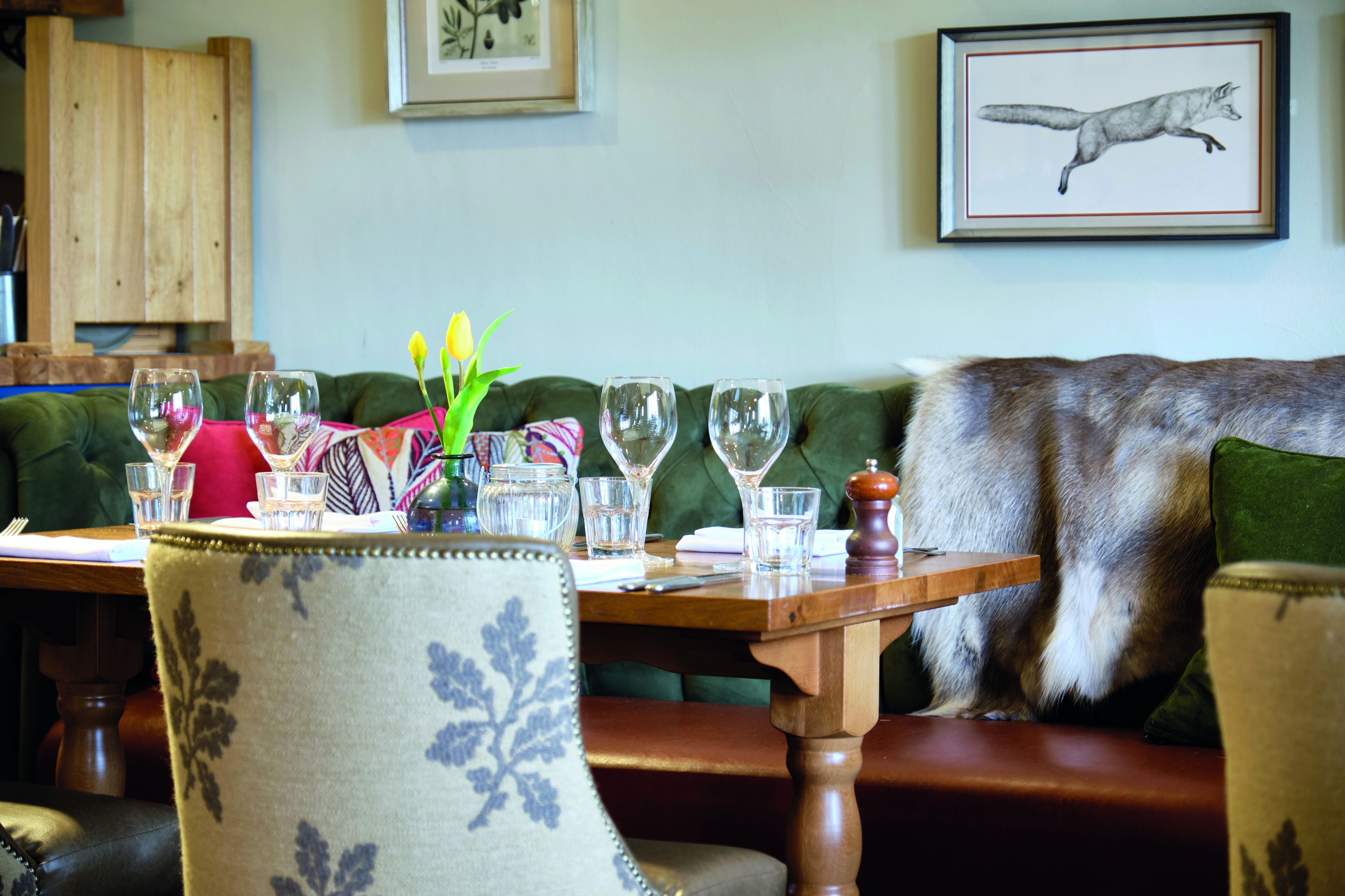 A dining area with a wooden table set for two, a green upholstered sofa, and a framed animal illustration on the wall.