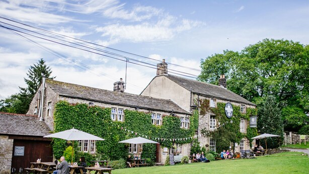 A traditional stone building with ivy-covered walls, outdoor seating, and a grassy lawn. - Lister Arms (Skipton)