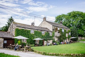 A traditional stone building with ivy-covered walls, outdoor seating, and a grassy lawn. - Lister Arms (Skipton)