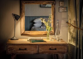 Un escritorio de madera con un espejo, libros, una lámpara y un jarrón con flores.