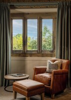 Una habitación con un ventanal grande, un sillón de cuero, una mesita redonda y un reposapiés a juego.