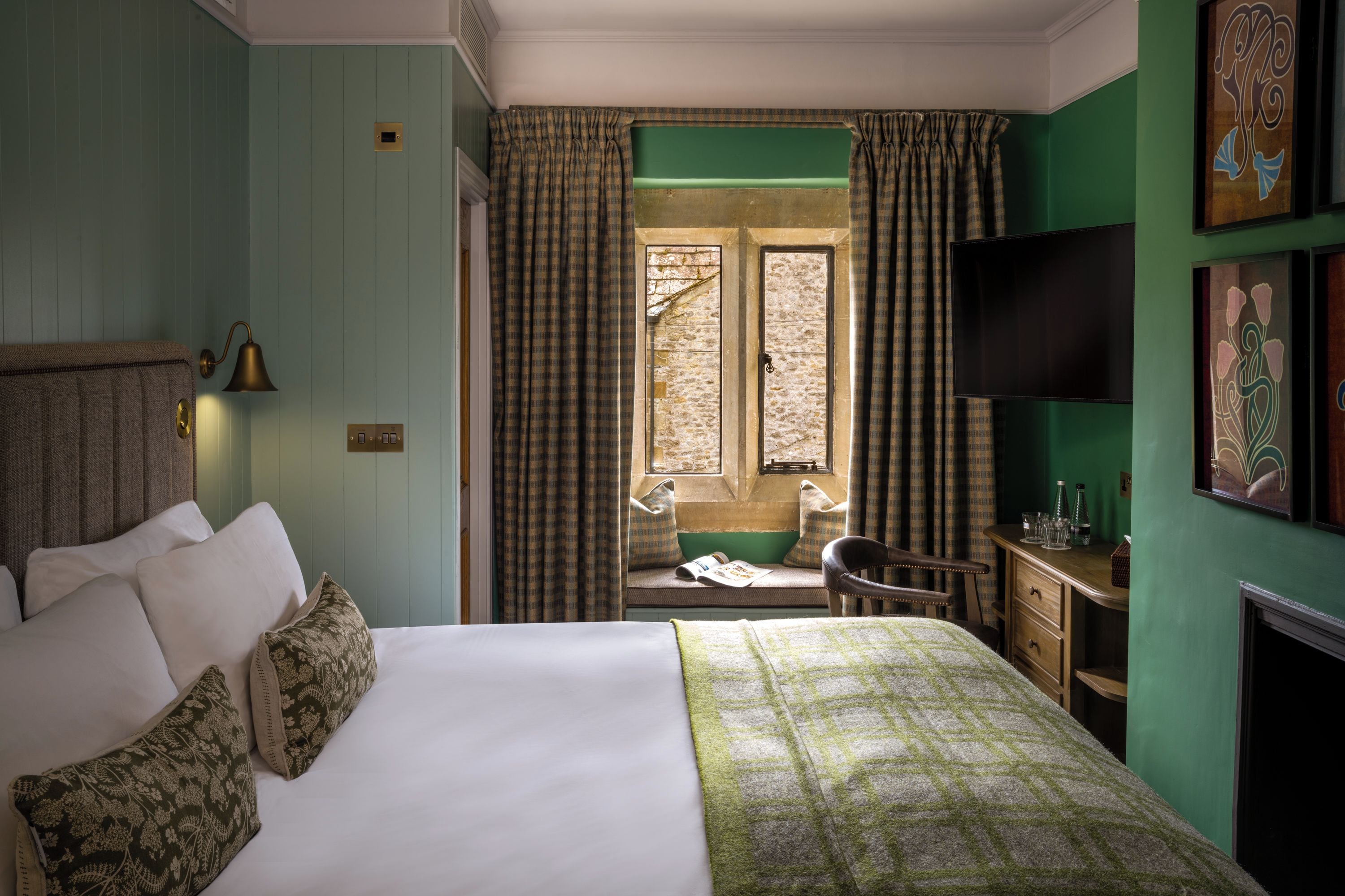 A hotel room with a bed, a desk, a chair, a television, and a window with curtains.