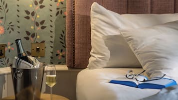 Una habitación de hotel con cama, mesita de noche, lámpara, una botella de champán y copas.