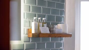 A shelf with toiletries and a glass of water against a tiled wall.