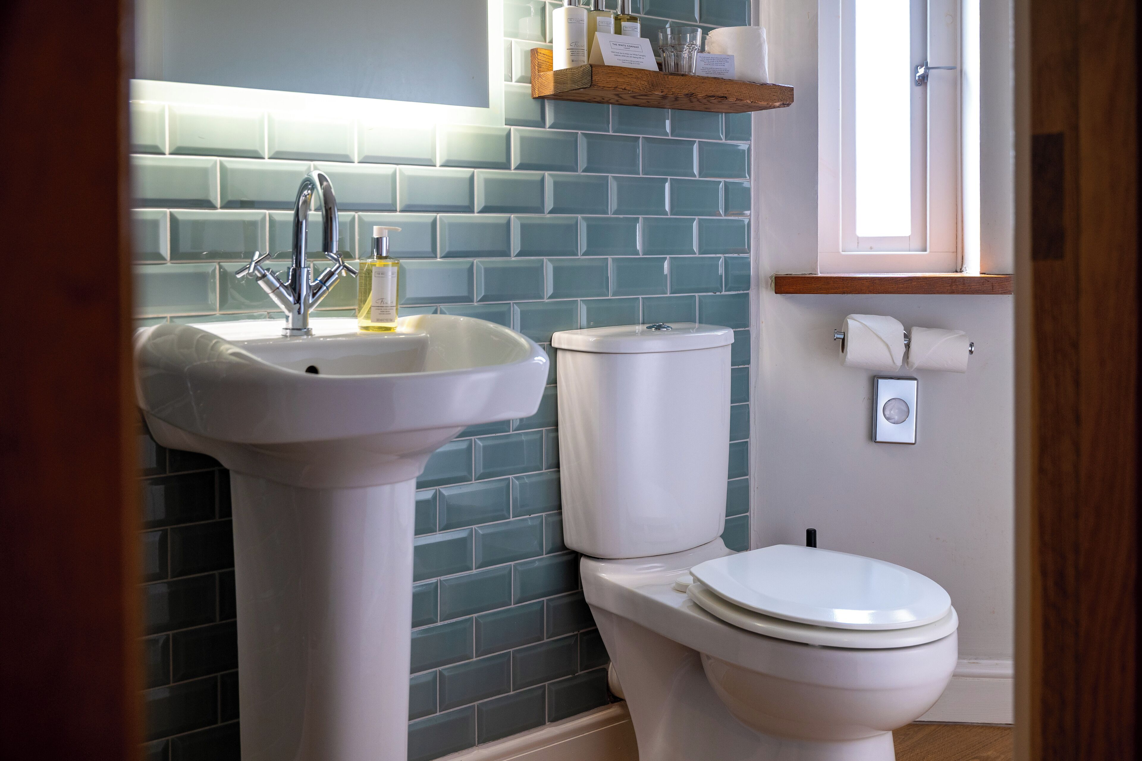 A bathroom with a white sink, a toilet, and a shelf above the toilet.