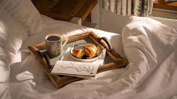 A neatly made bed with white linens, a tray with croissants, a cup of coffee, and a book on a wooden tray.