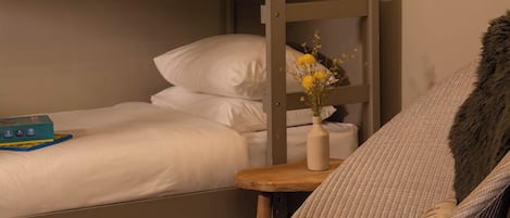 A bunk bed with white bedding, a small table with a vase of flowers, and a chair with a fur throw.