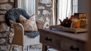 A wicker chair with a dog-themed pillow and a grey throw blanket. A wooden table with a teapot and jars is in the foreground. - Lister Arms (Skipton)