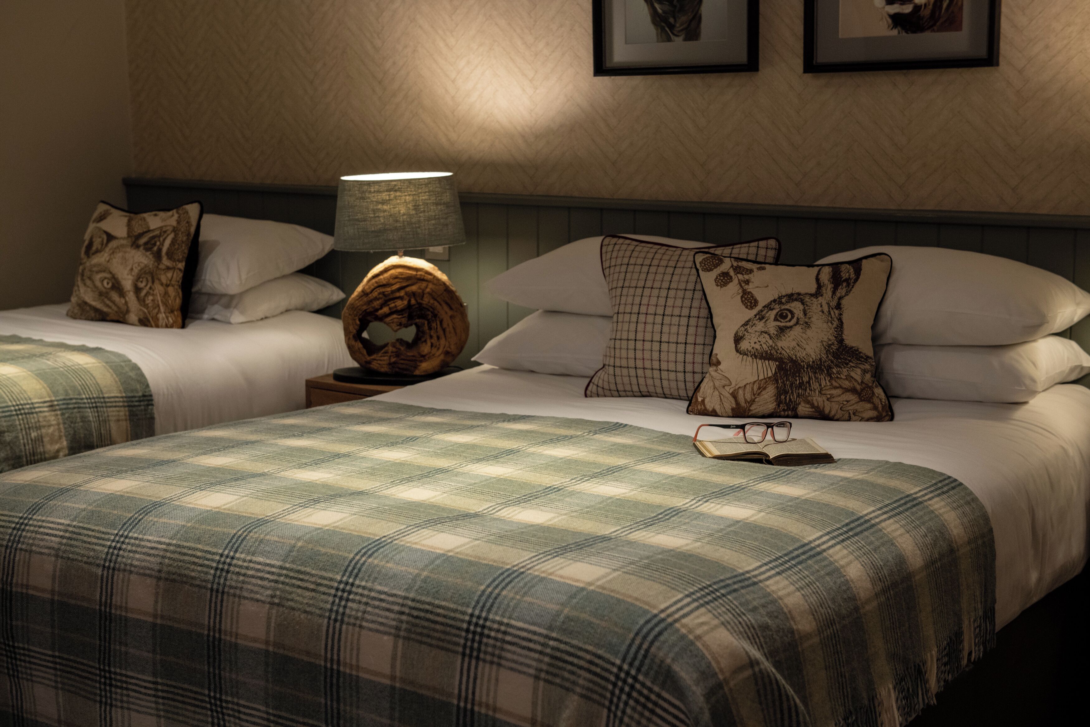 A hotel room with two beds, a nightstand with a lamp, and a wall with framed pictures.