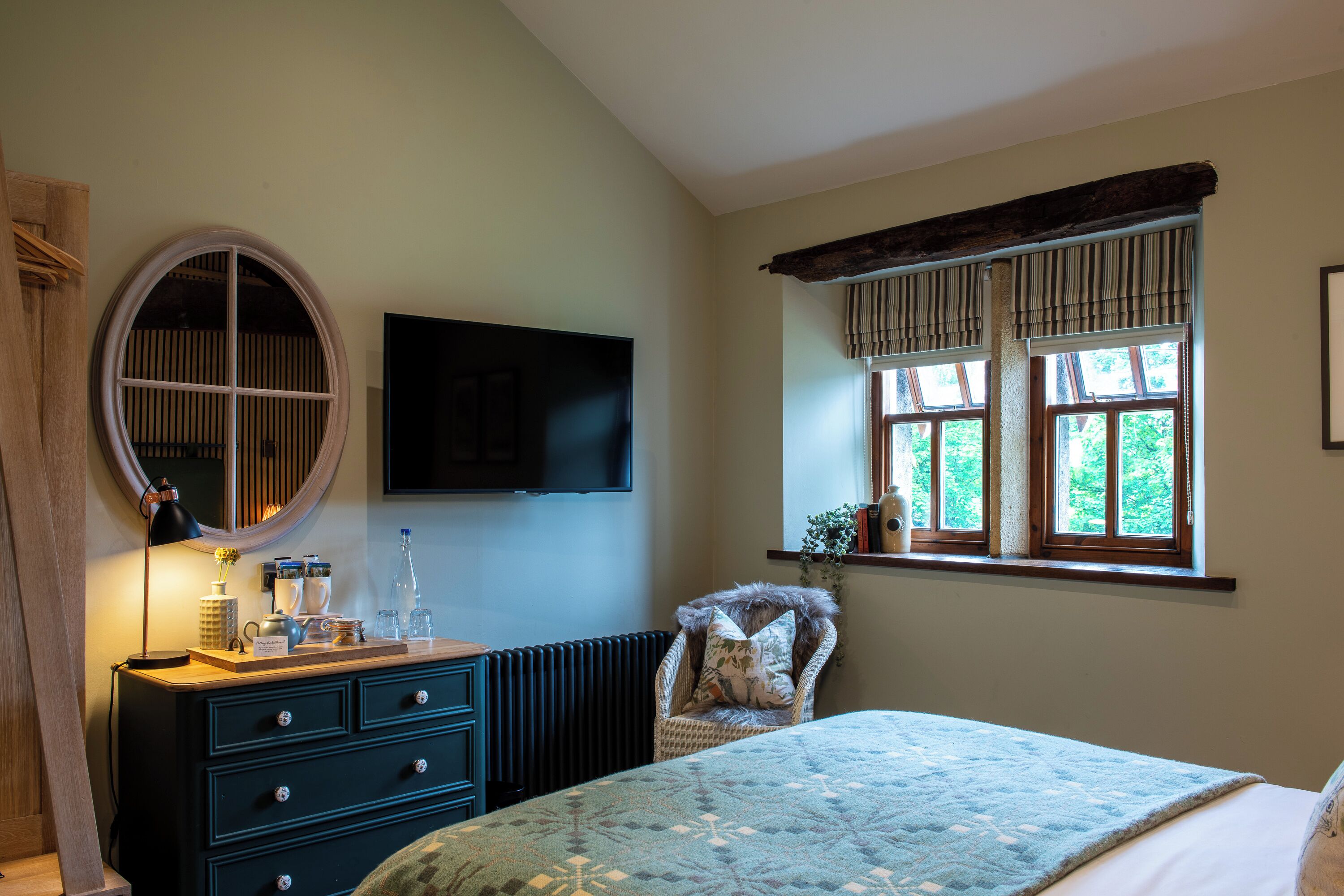 A bedroom with a bed, dresser, mirror, TV, and window with curtains.