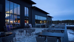 Een modern gebouw met grote ramen, terraszitplaatsen en een stenen patio.