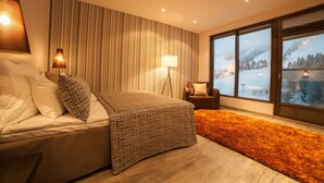 Een moderne slaapkamer met een bed, een nachtkastje, een lamp, en uitzicht op een besneeerd landschap door grote ramen, en een kamerkleed met dessin.