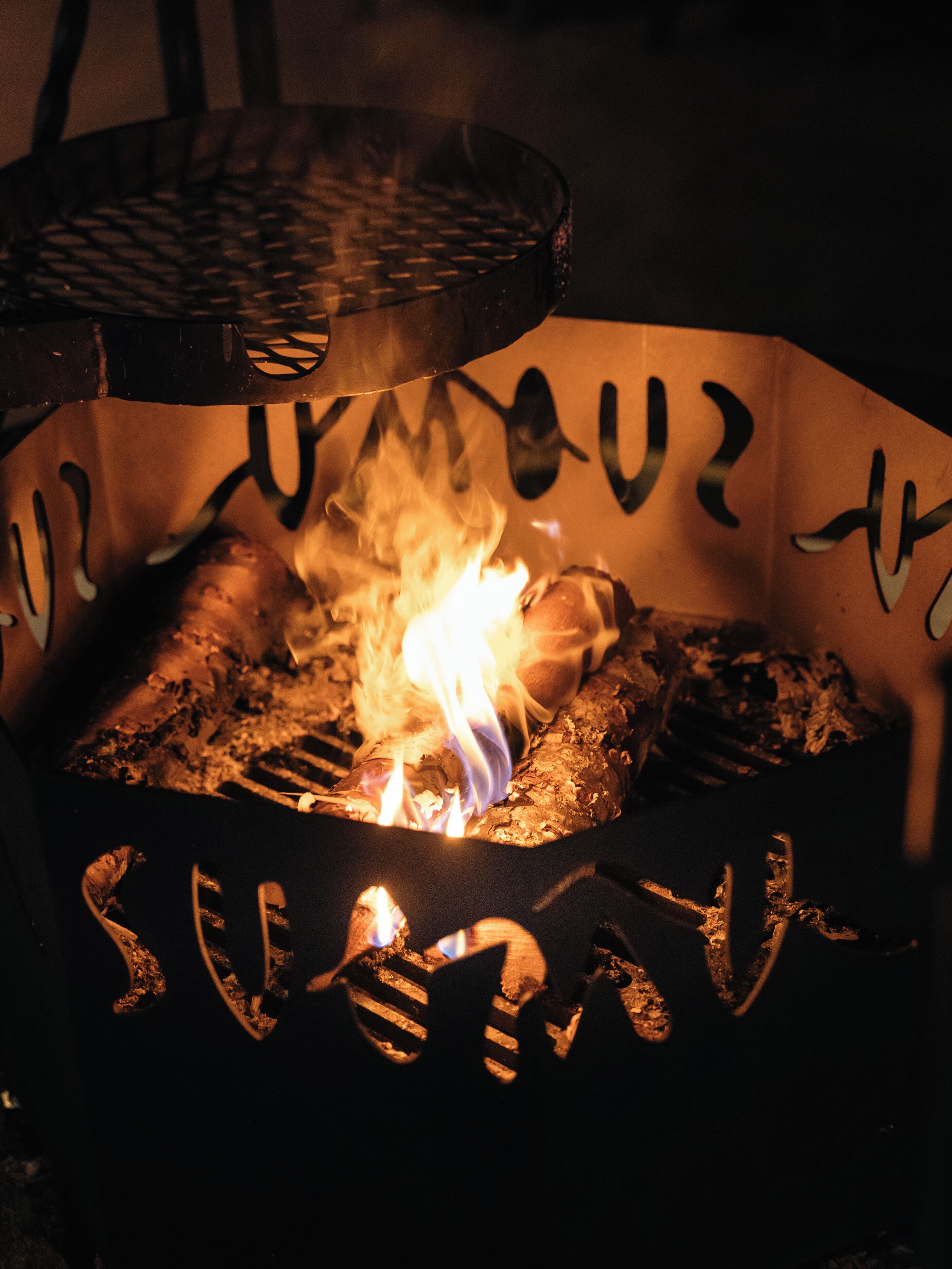 A grill with flames, surrounded by a metal structure with graffiti.