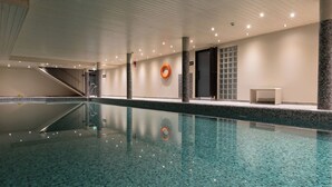Een binnenzwembad met helder water, een reddingsboei, een bankje en een trap naar een ander gedeelte.