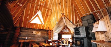 A log cabin interior with a stone fireplace, wooden benches, and a triangular window.