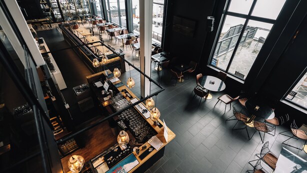 Een modern interieur met een bar, zitplaatsen en grote ramen.