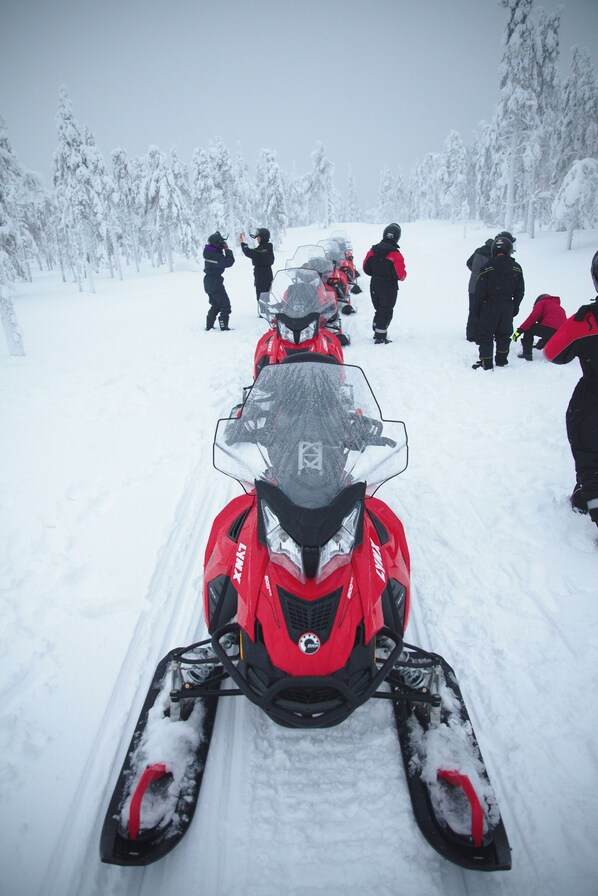 Un vehículo para nieve en un sendero nevado, con personas al fondo.