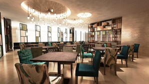 A modern dining area with tables and chairs, a chandelier, and a bookshelf. - Mercure Jakarta Cikini (Jakarta)