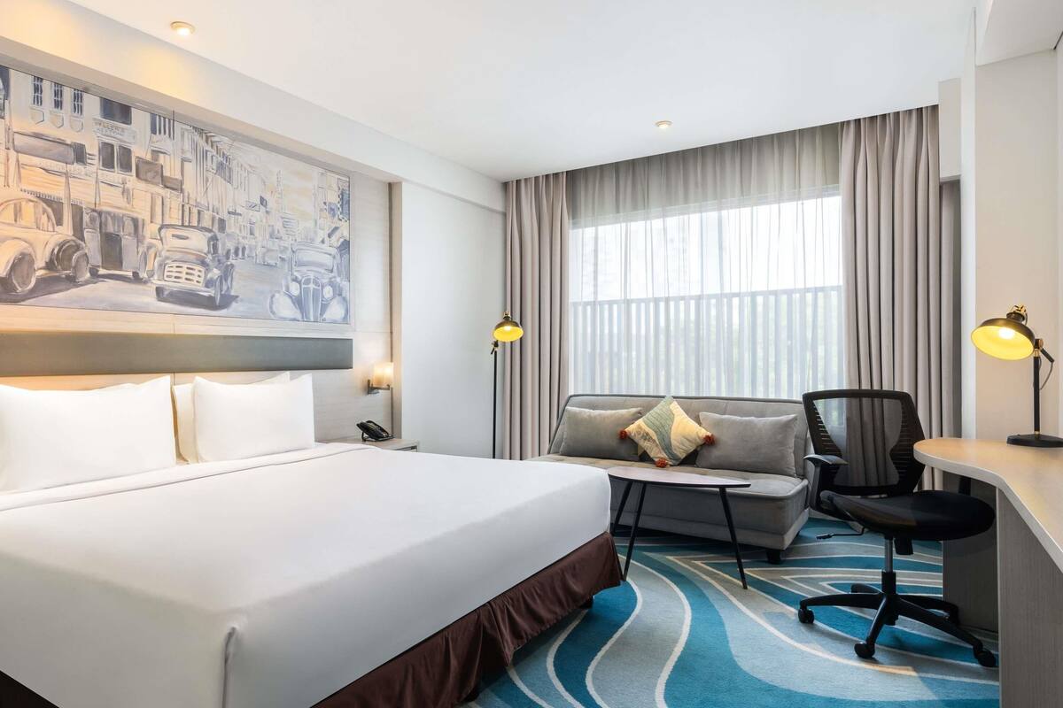 Habitación de hotel con una cama grande, un escritorio, una silla, un sofá y un cuadro en la pared.
