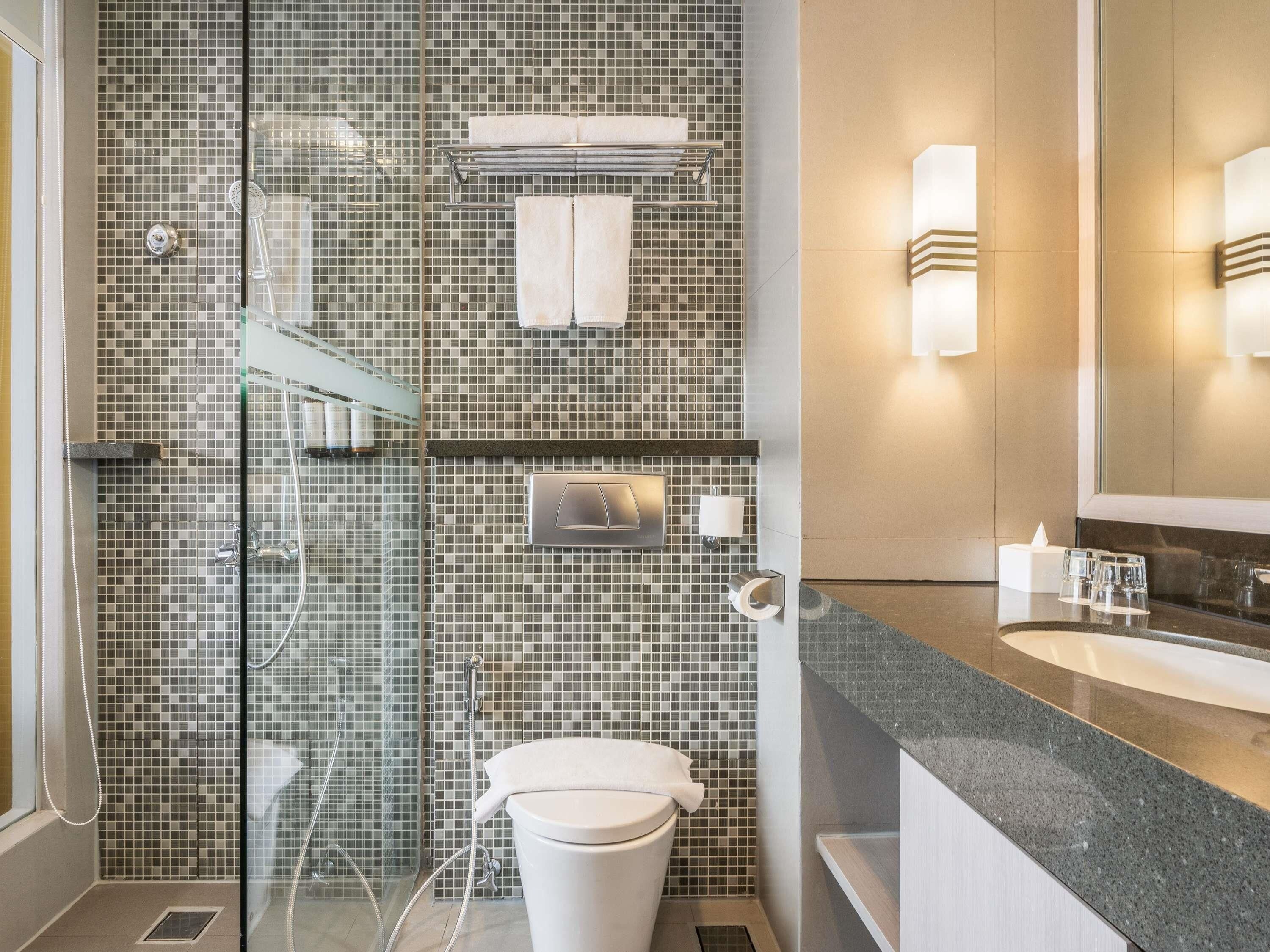 A modern bathroom with a glass shower enclosure, a toilet, a sink with a mirror, and a towel rack.