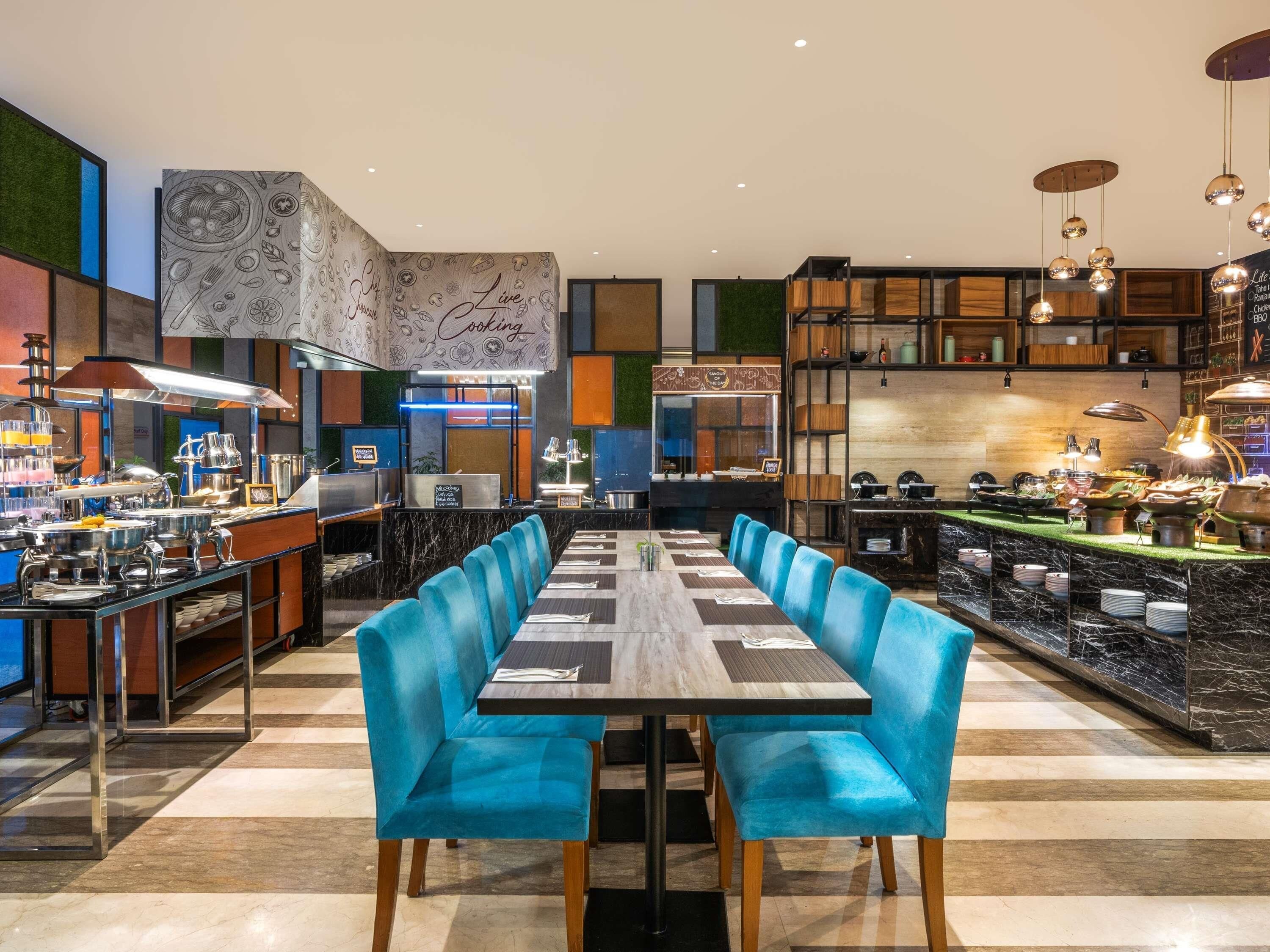 Un restaurante moderno con una larga mesa de comedor, sillas tapizadas en azul y diversos equipos de cocina.