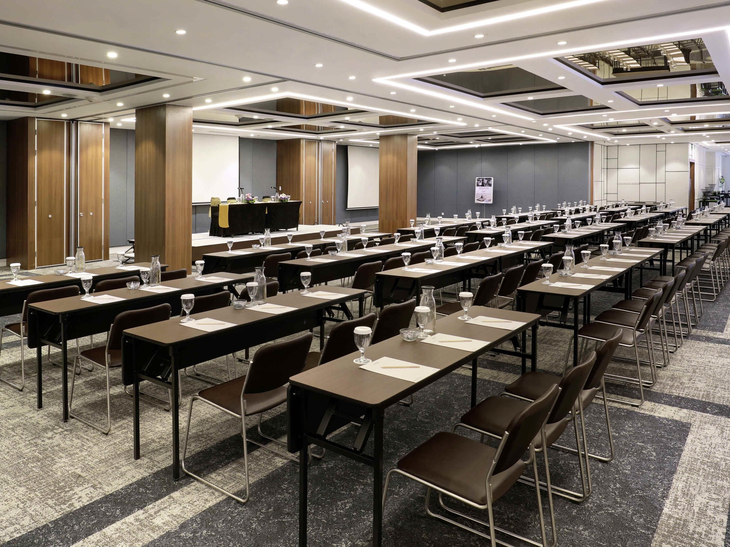 A conference room with multiple tables, chairs, and a stage with a podium.