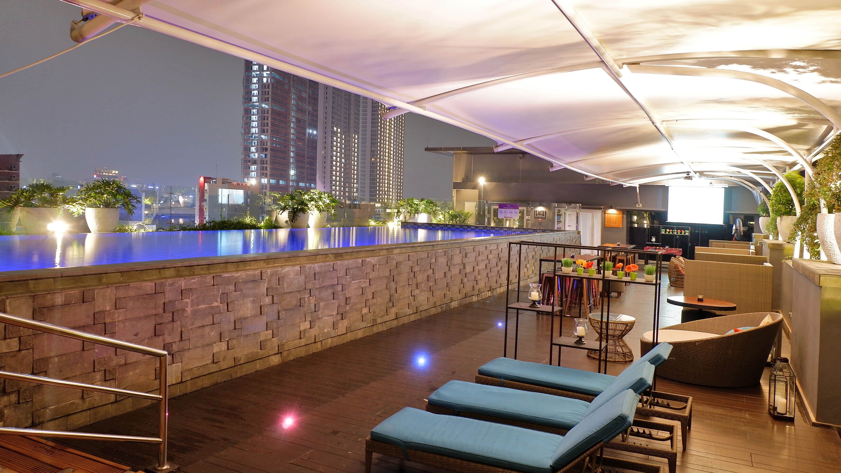 A rooftop bar with a pool, lounge chairs, and a bar area with seating and plants.