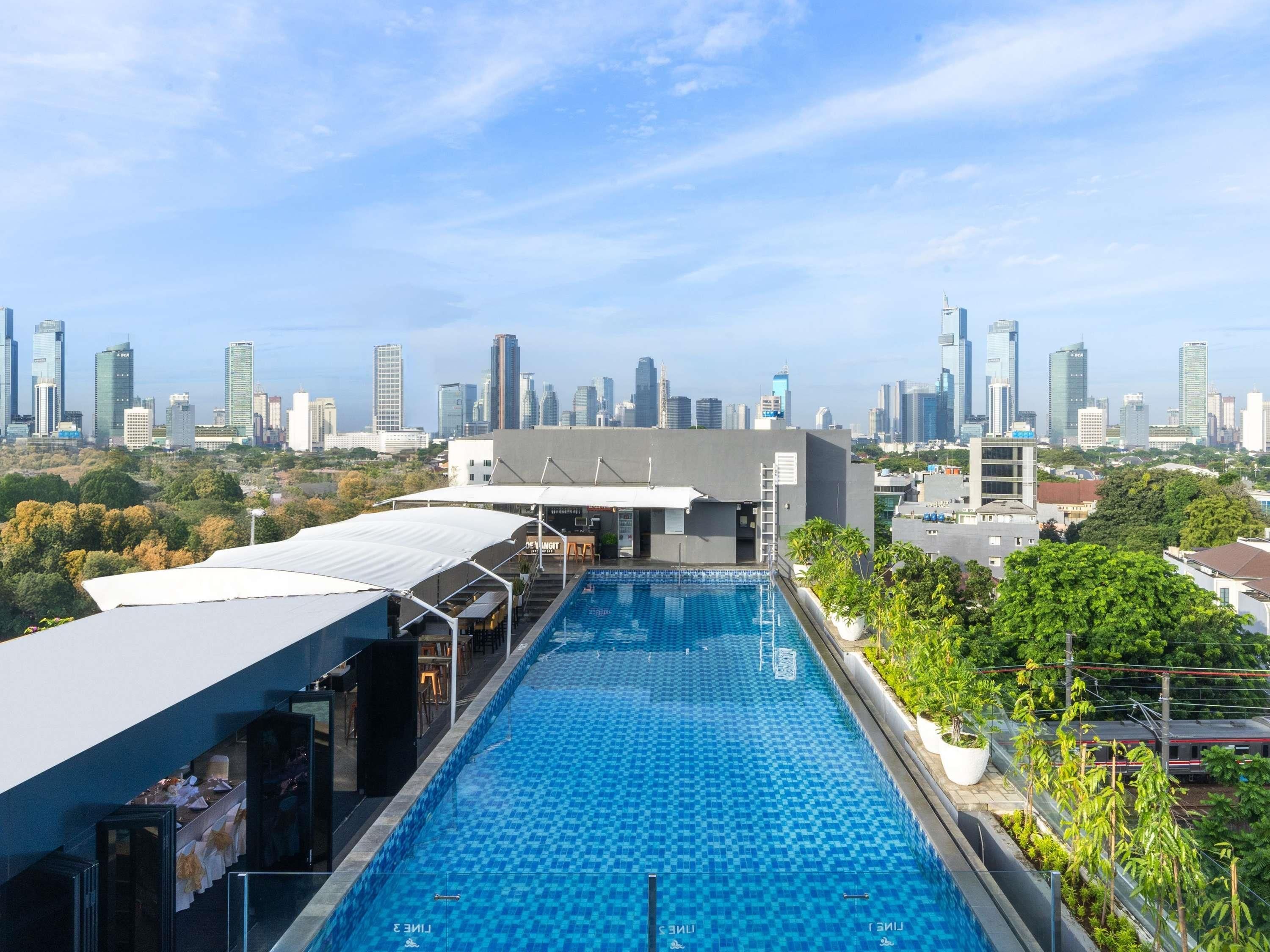 A rooftop swimming pool with a city skyline view, a covered seating area, and a bar/lounge with outdoor seating.