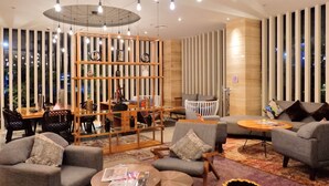 A modern lounge area with sofas, a wooden bookshelf, and a dining table. - Mercure Jakarta Cikini (Jakarta)