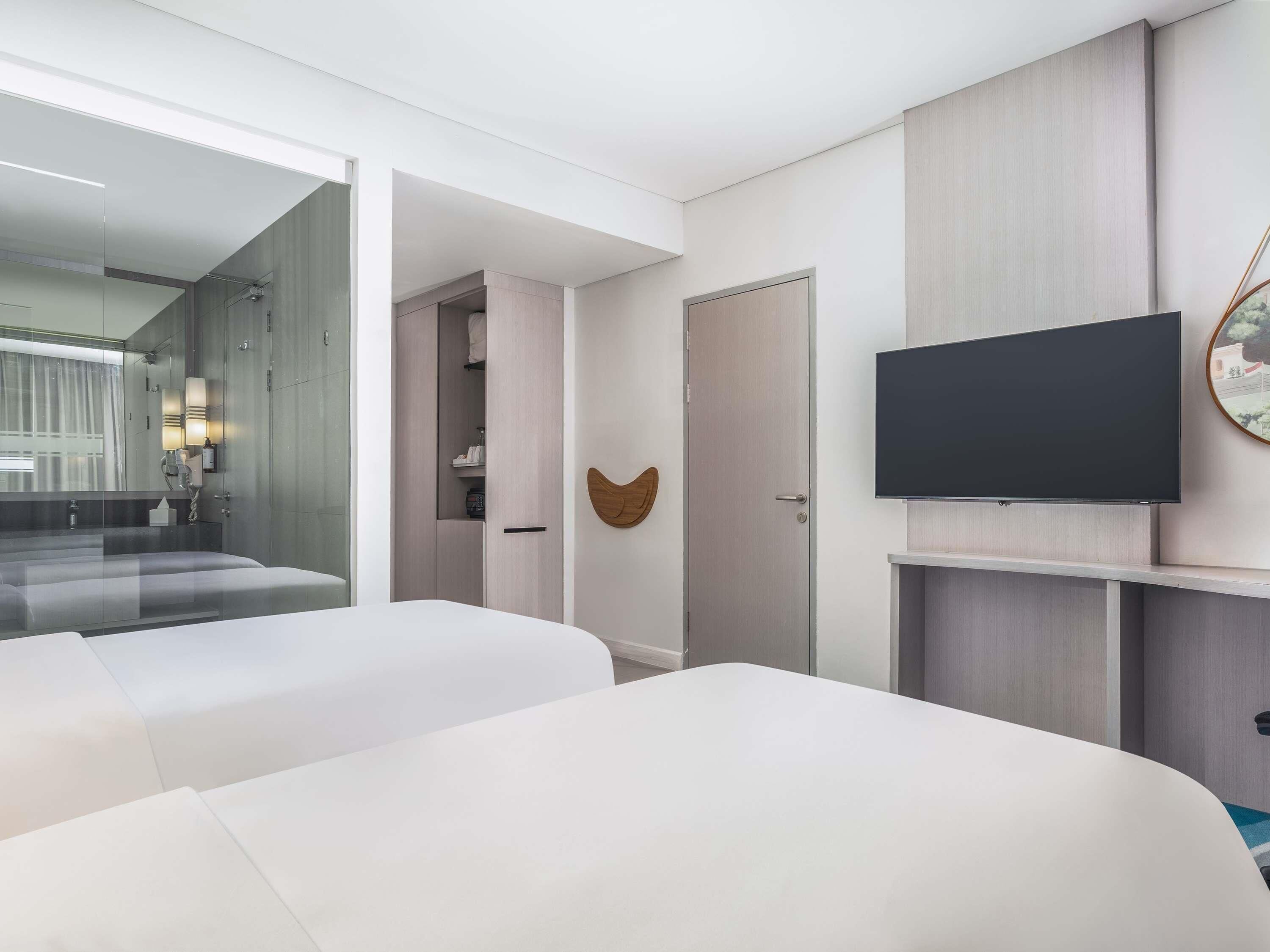 Et hotelværelse med to senge, et fjernsyn, et spejl og en garderobe.